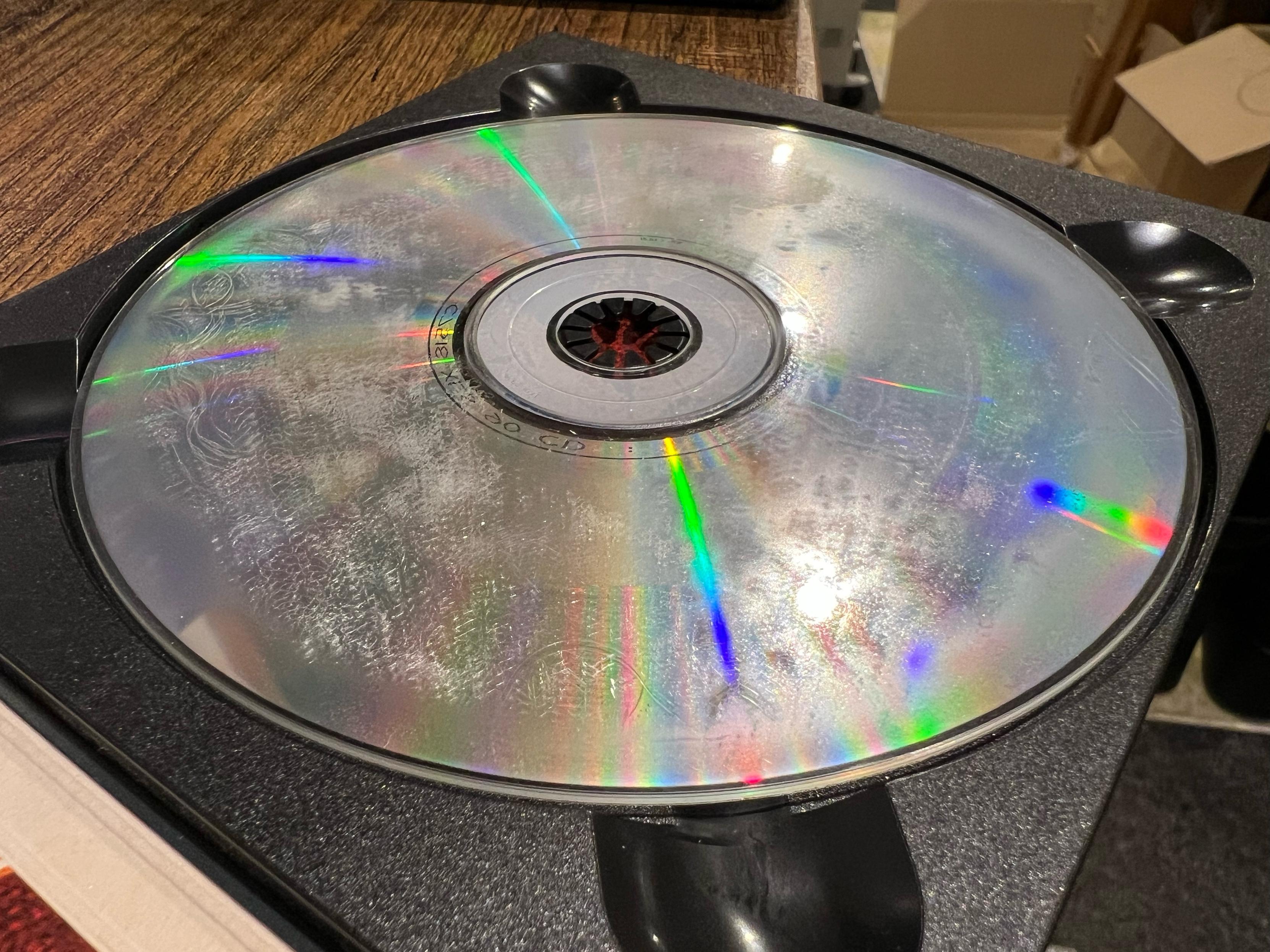 A photo of a CD with the print side downwards showing the music side. The surface of the CD is all foggy and blotchy, with some wavy lines towards the left as well.