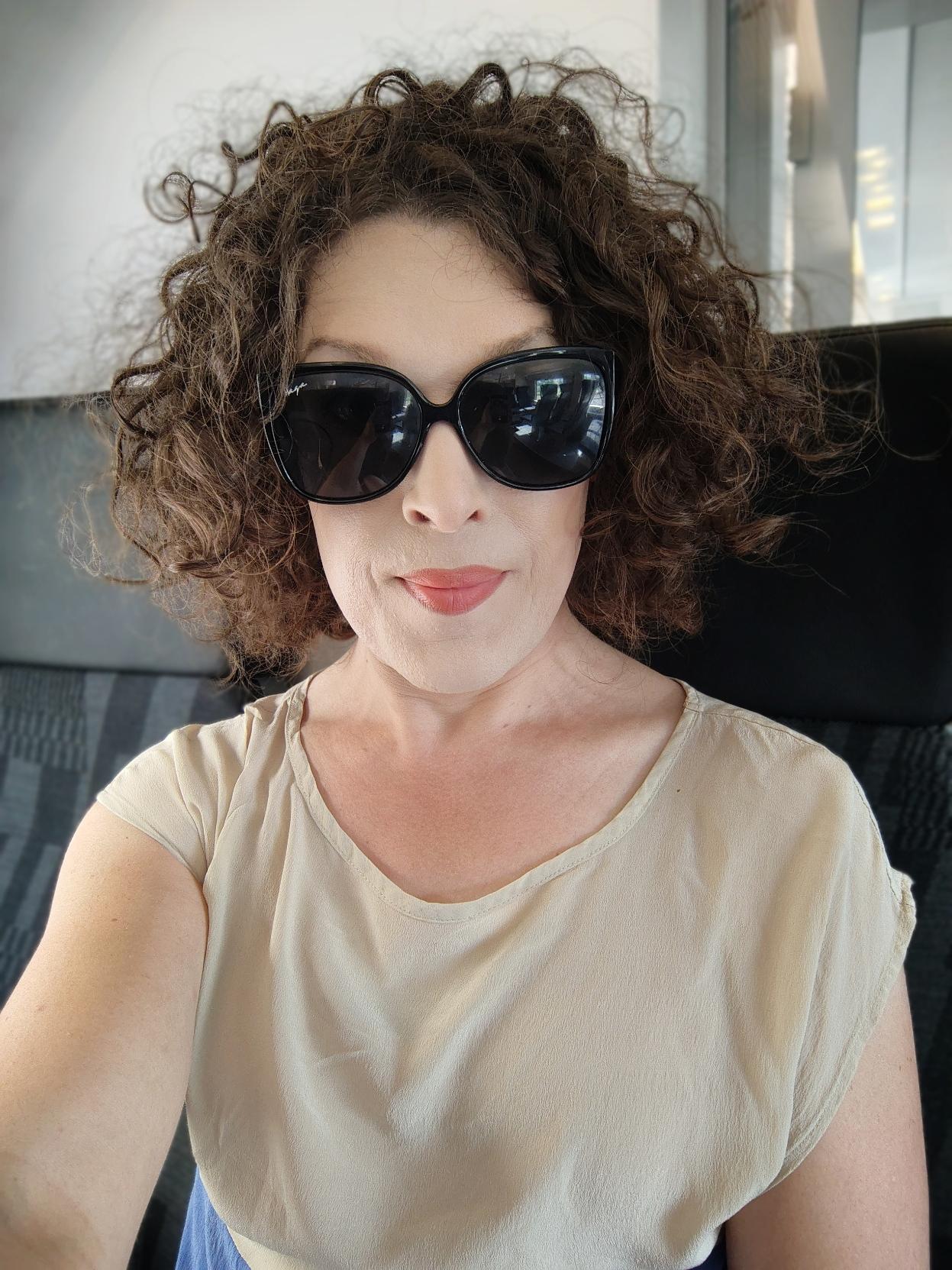 selfie of me in sunglasses on an x61, smiling, curly brown hair quite disorderly, and wearing a thin and loose light beige silk top
