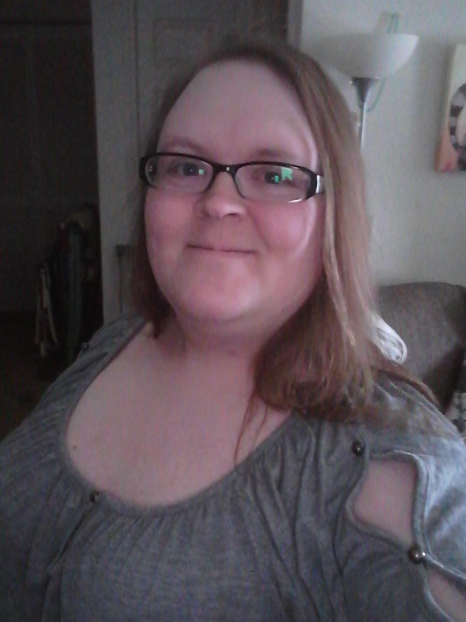 A selfie of a smiling white feminine entity. Ze's wearing a grey shirt with gap sleeves closed with silver buttons.