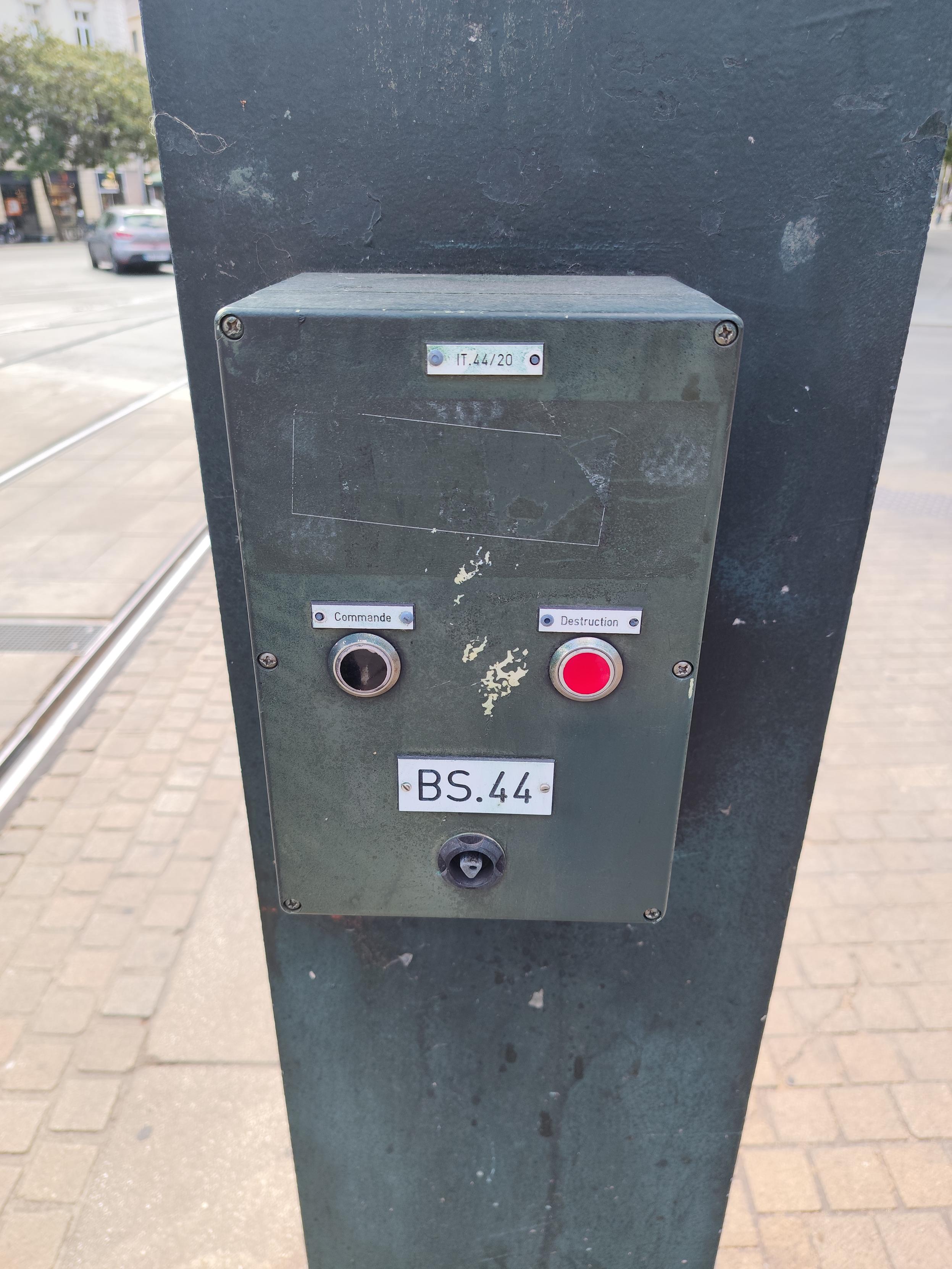 a metal box fitted to the side of a tram signal pole, it has 2 buttons, one black on the left labelled "command", the other red, on the right side, labelled "destruction"